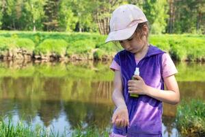 ragazza spruzza spray antizanzare sulla pelle in natura che le morde mani e piedi. protezione dalle punture di insetti, repellente sicuro per i bambini. attività ricreative all'aperto, contro le allergie. estate foto