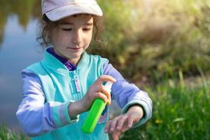 ragazza spruzza spray antizanzare sulla pelle in natura che le morde mani e piedi. protezione dalle punture di insetti, repellente sicuro per i bambini. attività ricreative all'aperto, contro le allergie. estate foto