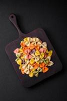 crudo farfalle pasta nel diverso colori su un' buio calcestruzzo sfondo foto