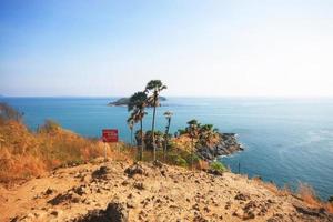 attenzione scivoloso avvertimento cartello su roccia montagna cape.bellissimo paesaggio marino con tramonto e palma albero su asciutto erba campo su montagna di phrom il p capo nel Phuket isola, Tailandia. foto