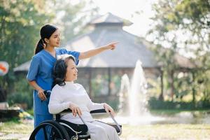 anziano asiatico anziano donna su sedia a rotelle con asiatico attento Caregiver. assistenza infermieristica casa ospedale giardino concetto. nel sole leggero foto