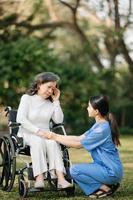 anziano asiatico anziano donna su sedia a rotelle con asiatico attento Caregiver. assistenza infermieristica casa ospedale giardino concetto. nel sole leggero foto