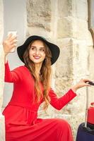 bellissimo giovane caucasico donna nel nero cappello guardare su il smartphone sorridente e seduta su le scale a il porta all'aperto. foto