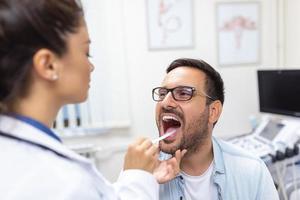 maschio paziente apertura il suo bocca per il medico per Guarda a il suo gola. femmina medico l'esame dolorante gola di paziente nel clinica. otorinolaringoiatra esamina dolorante gola di paziente. foto