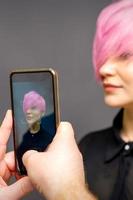uomo parrucchiere mani assunzione immagine su smartphone di sua cliente corto rosa acconciatura. foto