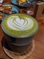 vicino su verde matcha latte macchiato al di sopra di il di legno tavolo su il bar e resto. il foto è adatto per uso per caffè negozio sfondo, menù manifesto e matcha soddisfare media.