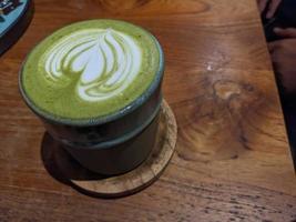 vicino su verde matcha latte macchiato al di sopra di il di legno tavolo su il bar e resto. il foto è adatto per uso per caffè negozio sfondo, menù manifesto e matcha soddisfare media.