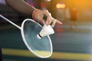 badminton giocatore indossa arcobaleno braccialetti e Tenere racchetta e bianca volano nel davanti di il netto prima servendo esso per giocatore nel un altro lato di il Tribunale, concetto per lgbt persone attività. foto