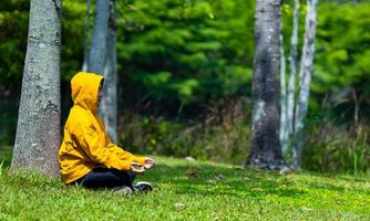 uomo nel giallo felpa con cappuccio è rilassante praticante meditazione nel il foresta per raggiungere felicità a partire dal interno pace saggezza per salutare mente e anima durante estate concetto foto