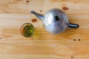un' tazza con verde tè e teiera su bianca di legno tavolo sfondo. foto