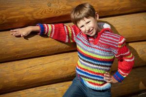 un' ragazzo di elementare età nel un' a strisce maglione su un' sfondo di un' di legno recinzione. foto