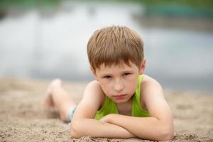 un' piccolo bambino nel il sabbia vicino il acqua. portret di un' ragazzo nel estate Abiti su il spiaggia. foto