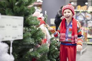 contento bambino a il Natale mercato. gioioso ragazzo su il sfondo di Natale i saldi nel il negozio. foto