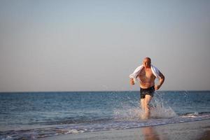 un anziano uomo corre lungo il spiaggia. foto