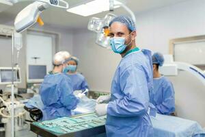 ritratto di contento uomo chirurgo in piedi nel operativo camera, pronto per opera su un' paziente. maschio medico lavoratore nel chirurgico uniforme nel operazione Teatro. foto