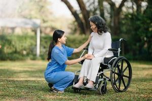 anziano asiatico anziano donna su sedia a rotelle con asiatico attento Caregiver. assistenza infermieristica casa ospedale giardino concetto. nel sole leggero foto