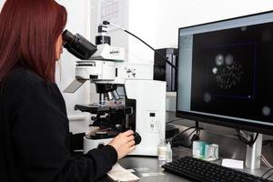 giovane femmina scienziato guardare a un' cellula nel metafase palcoscenico per rendere un' cariotipo nel il laboratorio foto