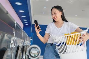 asiatico bellissimo donna sorridente contento fare faccende a il lavanderia utilizzando Telefono foto