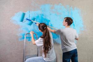 coppia nel nuovo casa durante riparazione lavori pittura parete insieme. contento famiglia Tenere dipingere rullo pittura parete con blu colore dipingere nel nuovo Casa. casa rinnovamento Fai da te rinnovare casa concetto. foto