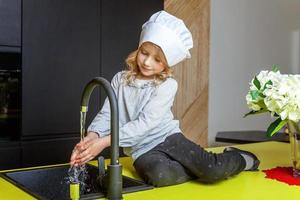 poco ragazza con capocuoco cappello apprendimento cucinando sorridente nel cucina foto