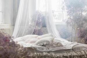 un' letto nel un' luminosa Camera da letto nel pastello colori nel boho stile, il trend colore di 2023. il camera è decorato con lilla e rosa gypsophila fiori, Vintage ▾ arredamento nel il camera nel retrò soffitta stile. foto