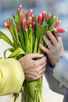 un' giovane coppia nel amore su il strada, Tenere fiori nel loro mani a un' romantico momento. un' uomo dà rosso tulipani per un' bionda donna.la concetto di il primavera vacanza è marzo 8, Pasqua, Da donna giorno foto