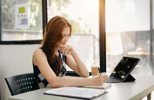 asiatico femmina Università alunno concentrandosi su sua in linea aula con tavoletta e il computer portatile foto