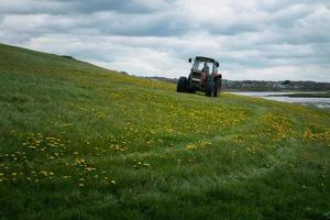 trattore guida su azienda agricola nel fiore campo di il silverstrand spiaggia nel Galway, Irlanda foto