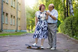 contento anziano coppia con un' skateboard. bello uomo e donna anziano cittadini. marito e moglie di vecchio età per un' camminare nel il città. foto