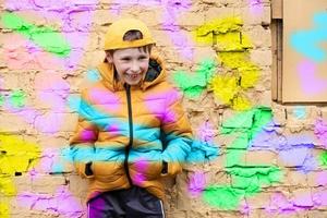 bambino nel graffiti. il ragazzo è in piedi contro un' mattone parete nel alla moda Abiti e un' baseball berretto, delineato con luminosa colori. foto