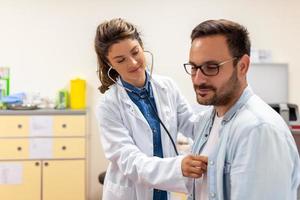 cura caucasico femmina medico uso fonendoscopio esaminare maschio paziente cuore Vota a consultazione nel Ospedale. donna infermiera o gp uso stetoscopio ascolta per uomo battito cardiaco nel clinica. foto