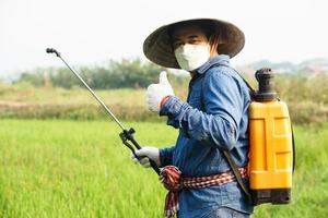 asiatico contadino è spruzzatura biologico fertilizzante a risaia campo. pollice su. concetto utilizzando amichevole Prodotto con ambiente agricoltura con no sostanze chimiche usando. sicurezza con utente e ambiente. foto