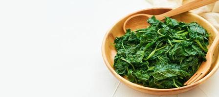 vicino su verde cucinare foglia spinaci insalata nel legna ciotola su bianca tavolo sfondo. le foglie spinaci o mucchio di spinaci cibo insalata foto