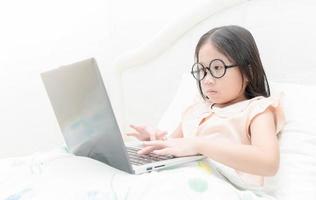 carino asiatico Lavorando su un' il computer portatile seduta su il letto foto