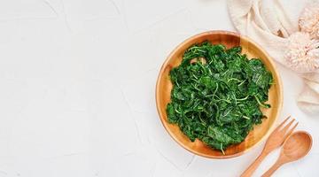 superiore Visualizza verde cucinare foglia spinaci insalata nel legna ciotola su bianca tavolo sfondo. le foglie spinaci o mucchio di spinaci cibo insalata sopra la testa, piatto posare foto