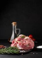 un' pezzo di Maiale prosciutto su un' nero tavola e spezie oliva olio, sale, rosmarino ramo e Pepe foto