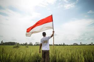 un' uomo Tenere un' rosso e bianca Indonesia bandiera su superiore di un' lussureggiante verde riso campo. ai generato foto