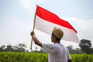 un' uomo Tenere un' rosso e bianca Indonesia bandiera su superiore di un' lussureggiante verde riso campo. ai generato foto