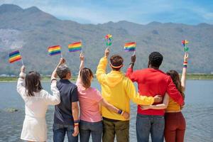 indietro Visualizza. giovane diversità persone Tenere gay orgoglio arcobaleno bandiera su il spiaggia contro il cielo. amore momento la spesa bene tempo insieme. LGBTQ concetto foto