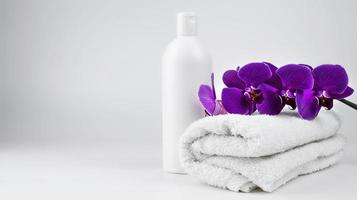 un' leggero lanciato asciugamano e un' bianca vaso di crema sapone. viola orchidea ramo su un' asciugamano. foto