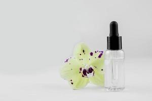 cosmetico siero nel un' trasparente bottiglia con un' pipetta. siero bottiglia su bianca sfondo. orchidea con bottiglia. foto