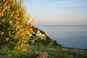 paesaggio marino con fiori, un campo erboso e una chiesa vicino a uno specchio d'acqua con un colorato cielo nuvoloso foto