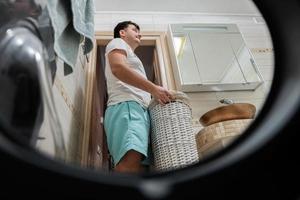 uomo con cestino, Visualizza a partire dal lavaggio macchina dentro. maschio fa lavanderia quotidiano routine. foto