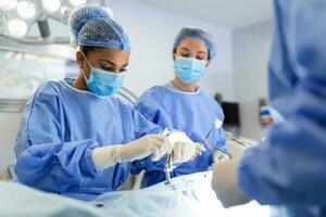 concentrato femmina chirurgo l'esecuzione chirurgia con sua squadra nel ospedale operativo camera. medici durante chirurgia nel operazione Teatro. foto