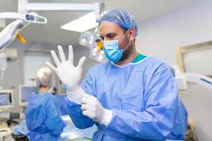 ritratto di maschio medico chirurgo mettendo su medico guanti in piedi nel operazione camera. chirurgo a moderno operativo camera foto
