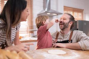 mamma e papà nel il cucina di il Casa con loro piccolo bambini. avere un' bene tempo cottura al forno pane e fabbricazione cena insieme. foto