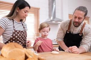 mamma e papà nel il cucina di il Casa con loro piccolo bambini. avere un' bene tempo cottura al forno pane e fabbricazione cena insieme. foto