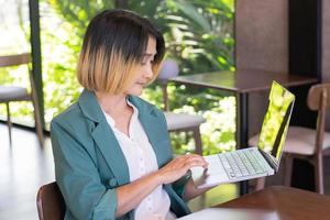 donna d'affari indossare un' completo da uomo verde Tenere il computer portatile e seduta nel il bar mentre in attesa per il ordinato caffè in attesa per clienti. foto