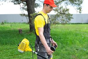 un' maschio giardiniere falcia il verde erba di il prato nel il Giardino dietro la casa con un' benzina tosaerba. trimmer per il cura di un' giardino tracciare foto