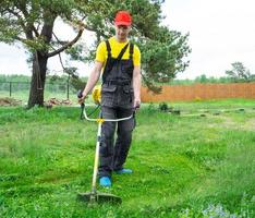 un' maschio giardiniere falcia il verde erba di il prato nel il Giardino dietro la casa con un' benzina tosaerba. trimmer per il cura di un' giardino tracciare foto